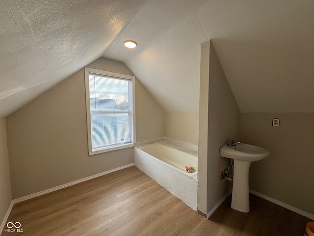 bathroom featuring hardwood / wood-style flooring, a tub to relax in, lofted ceiling, and a textured ceiling