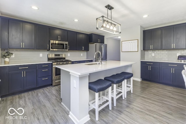 kitchen with appliances with stainless steel finishes, decorative light fixtures, a kitchen island with sink, light wood-type flooring, and a breakfast bar