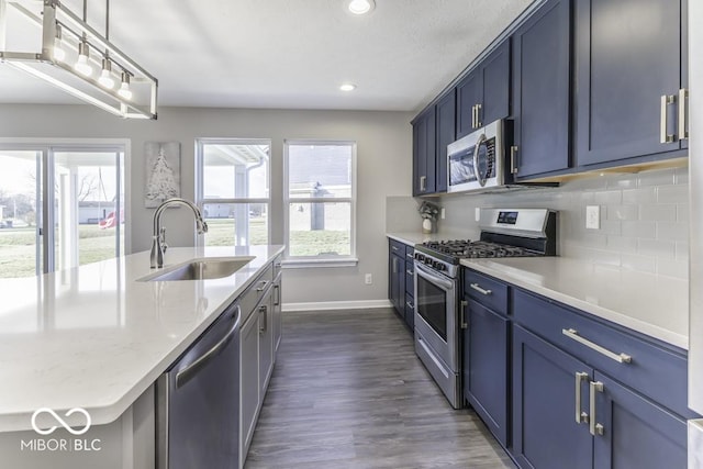 kitchen with pendant lighting, stainless steel appliances, sink, backsplash, and blue cabinets