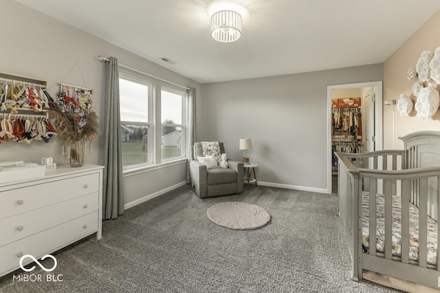 bedroom featuring dark carpet, a nursery area, a closet, and a walk in closet