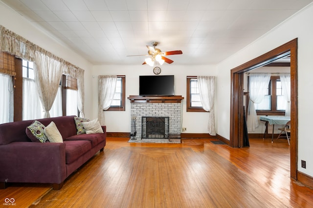 living room with ceiling fan, a healthy amount of sunlight, wood-type flooring, and a brick fireplace