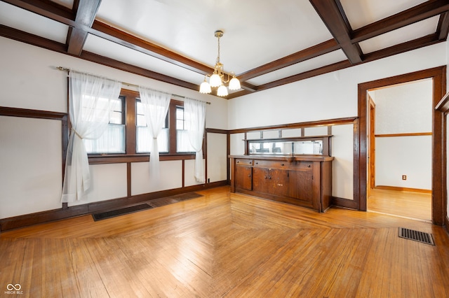 empty room with beamed ceiling, coffered ceiling, a chandelier, and light hardwood / wood-style floors