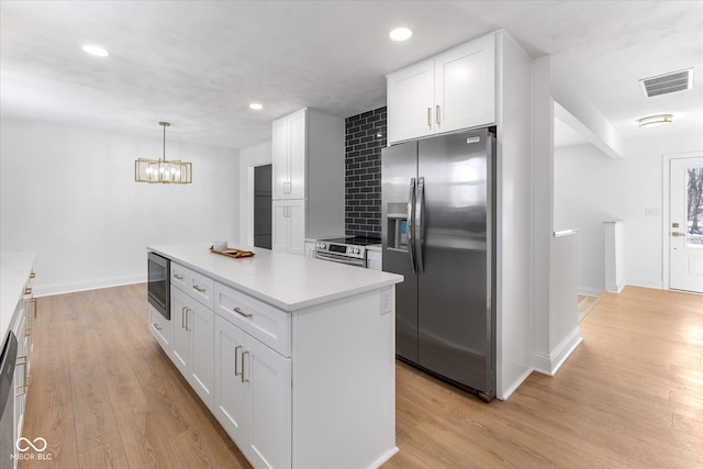 kitchen with pendant lighting, light wood-type flooring, tasteful backsplash, white cabinetry, and stainless steel appliances