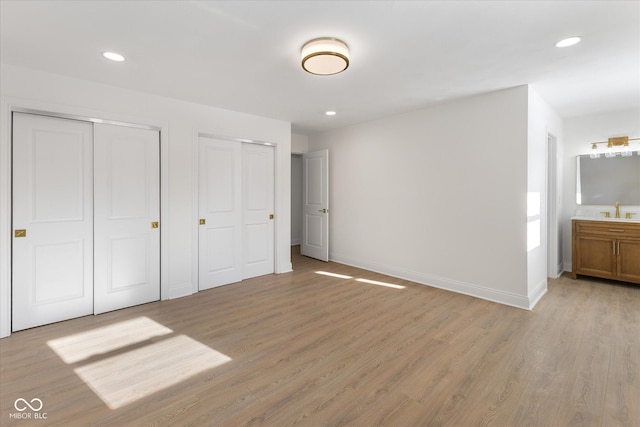 unfurnished bedroom with ensuite bath, light hardwood / wood-style floors, sink, and two closets