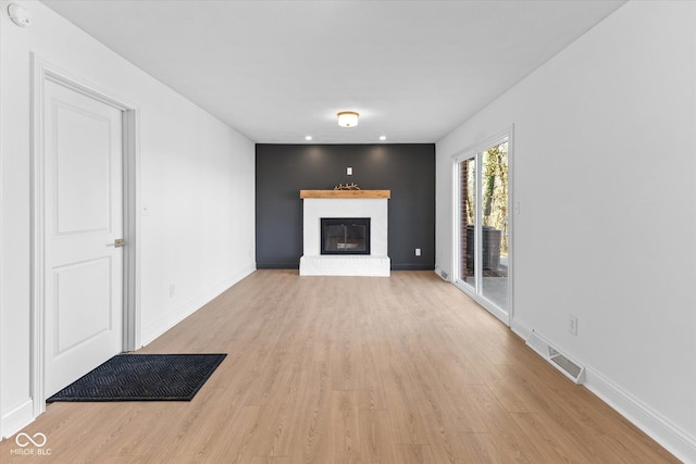 unfurnished living room with light wood-type flooring and a brick fireplace