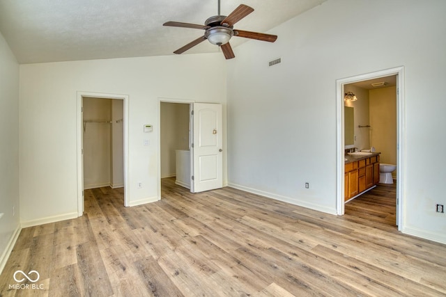 unfurnished bedroom featuring ceiling fan, connected bathroom, a closet, a walk in closet, and light hardwood / wood-style flooring