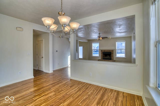 interior space featuring ceiling fan with notable chandelier, wood-type flooring, a textured ceiling, and a fireplace