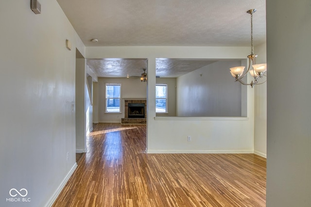 unfurnished living room with hardwood / wood-style flooring, a textured ceiling, a brick fireplace, and ceiling fan