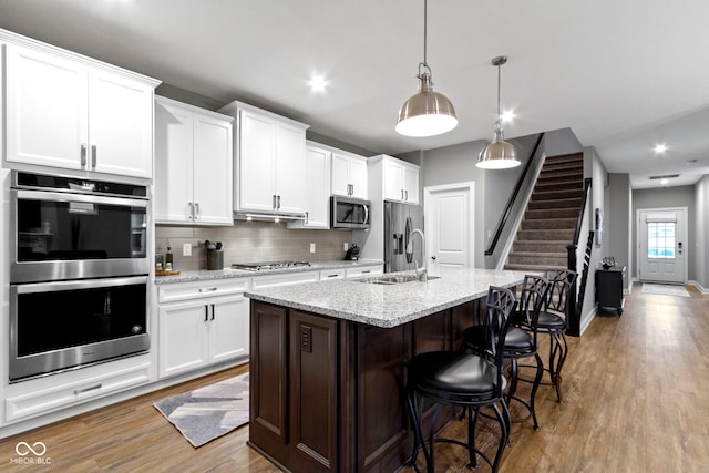 kitchen featuring white cabinets, sink, hanging light fixtures, an island with sink, and stainless steel appliances