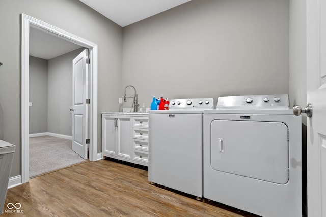 laundry area featuring washer and clothes dryer, cabinets, sink, and light hardwood / wood-style flooring