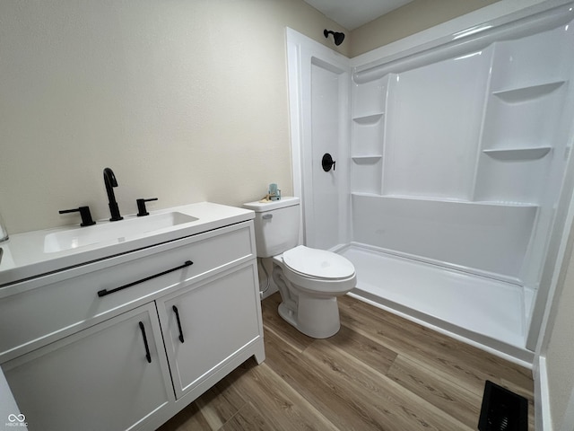 bathroom featuring wood-type flooring, vanity, toilet, and walk in shower