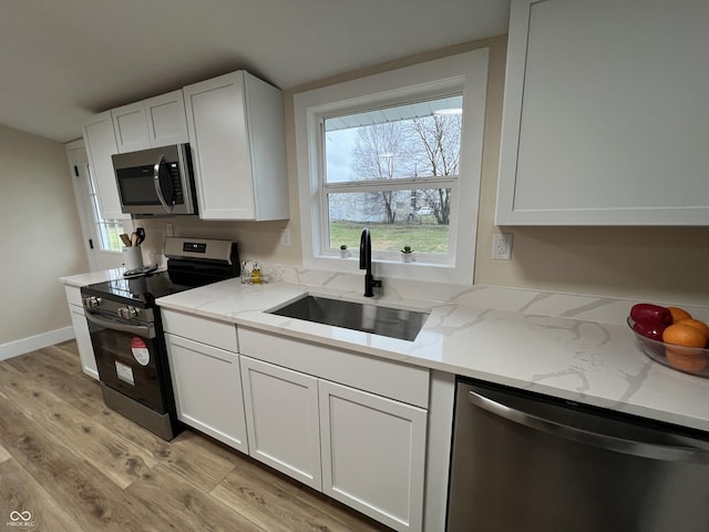 kitchen featuring white cabinets, sink, light stone countertops, appliances with stainless steel finishes, and light hardwood / wood-style floors