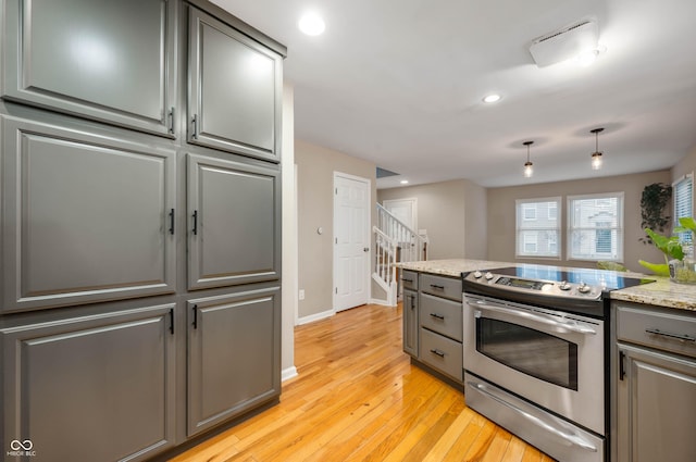 kitchen featuring stainless steel electric range oven, light stone countertops, and light wood-type flooring