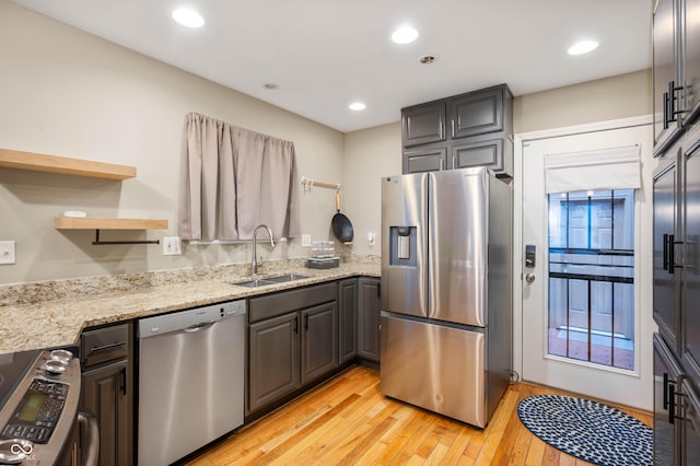 kitchen with light stone countertops, appliances with stainless steel finishes, light hardwood / wood-style floors, and sink