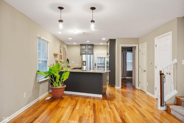 kitchen with light stone counters, kitchen peninsula, stainless steel fridge, light hardwood / wood-style floors, and decorative light fixtures