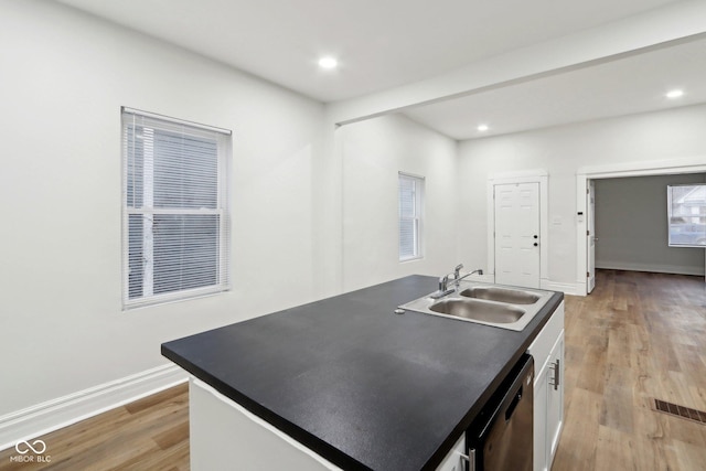kitchen featuring white cabinets, dark countertops, stainless steel dishwasher, a sink, and light wood-type flooring