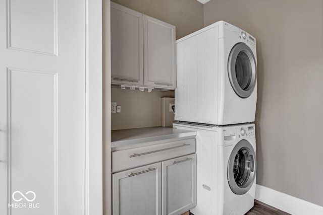 clothes washing area with stacked washer / dryer, cabinets, and dark hardwood / wood-style floors