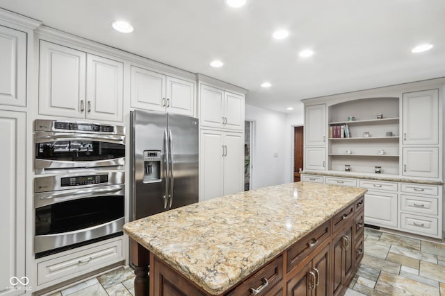 kitchen with light stone counters, dark brown cabinets, stainless steel appliances, white cabinets, and a kitchen island