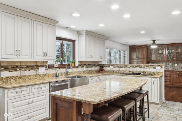 kitchen featuring black electric cooktop, ceiling fan, sink, a kitchen island, and a breakfast bar area