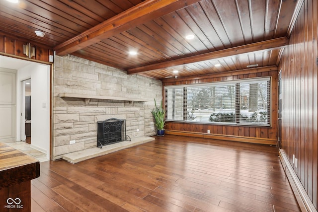 unfurnished living room with a baseboard heating unit, wooden ceiling, wooden walls, and beam ceiling