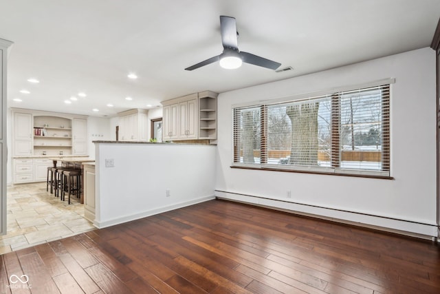 interior space featuring kitchen peninsula, hardwood / wood-style flooring, ceiling fan, and a baseboard heating unit