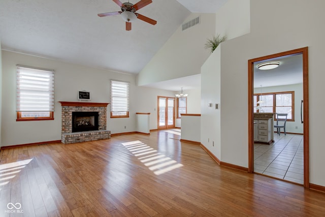 unfurnished living room with a brick fireplace, ceiling fan with notable chandelier, light hardwood / wood-style flooring, and high vaulted ceiling