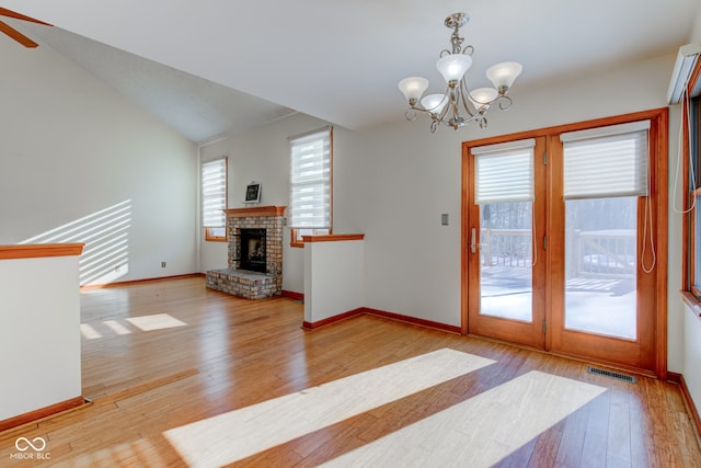 living room featuring vaulted ceiling, a brick fireplace, ceiling fan with notable chandelier, and light hardwood / wood-style flooring