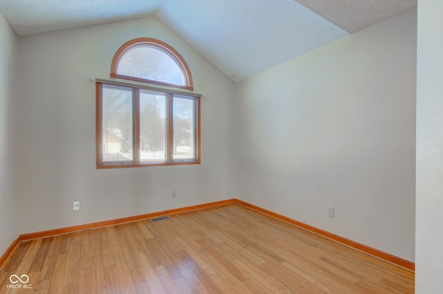 empty room featuring lofted ceiling, a textured ceiling, and light hardwood / wood-style flooring