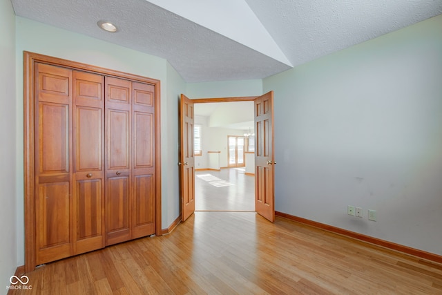 unfurnished bedroom with vaulted ceiling, a closet, a textured ceiling, and light hardwood / wood-style floors