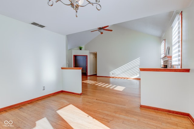 empty room featuring vaulted ceiling, ceiling fan with notable chandelier, and light hardwood / wood-style flooring