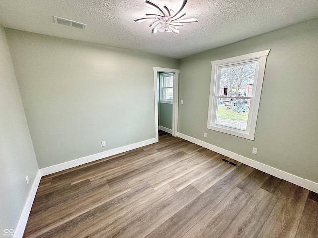 spare room featuring light hardwood / wood-style flooring, a textured ceiling, and an inviting chandelier