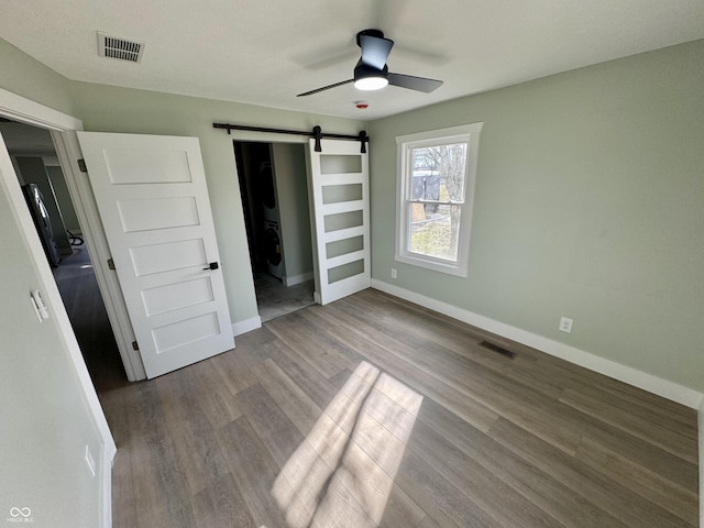 unfurnished bedroom featuring hardwood / wood-style floors, ceiling fan, and a barn door