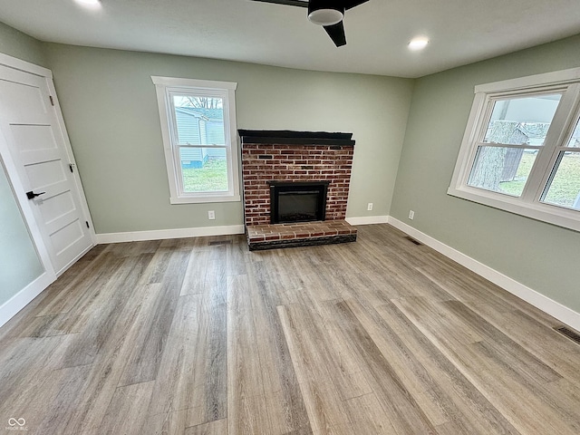 unfurnished living room with ceiling fan, a fireplace, and light hardwood / wood-style floors