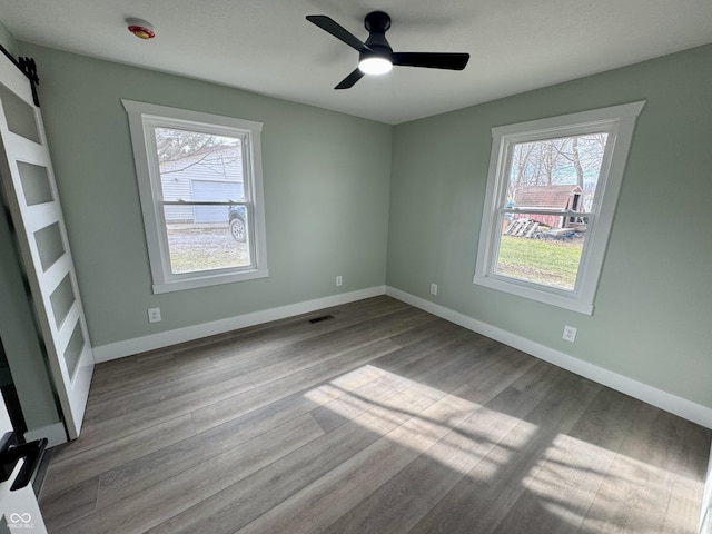 unfurnished room with light wood-type flooring, a barn door, and ceiling fan