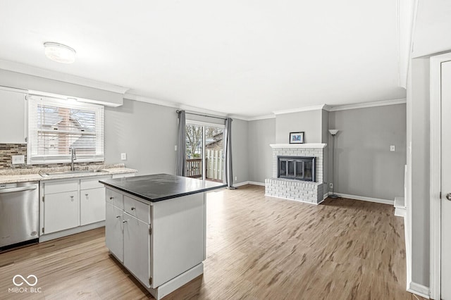 kitchen with white cabinets, sink, a brick fireplace, stainless steel dishwasher, and a kitchen island