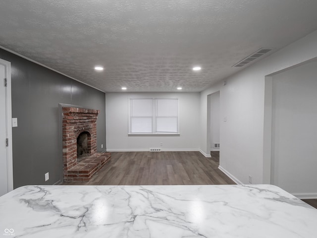 unfurnished living room with hardwood / wood-style flooring, a textured ceiling, and a brick fireplace