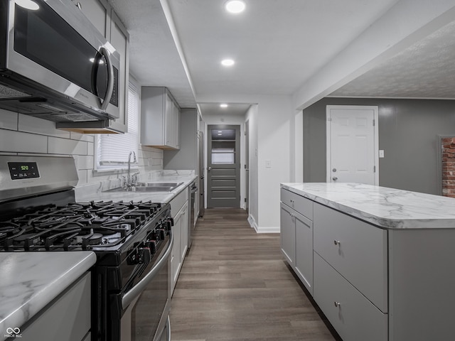 kitchen featuring sink, tasteful backsplash, gray cabinets, appliances with stainless steel finishes, and hardwood / wood-style flooring