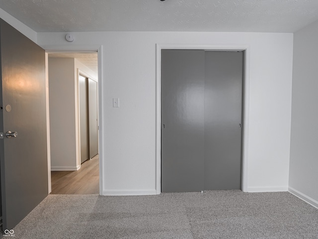 unfurnished bedroom with light colored carpet, a textured ceiling, and a closet