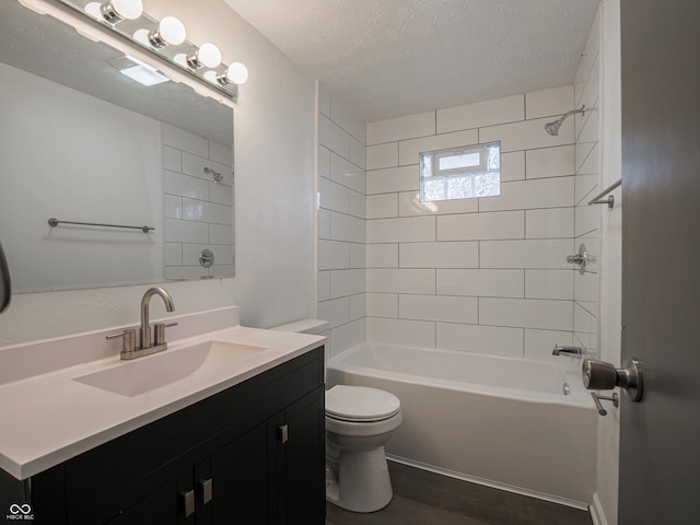 full bathroom with hardwood / wood-style floors, vanity, tiled shower / bath combo, toilet, and a textured ceiling