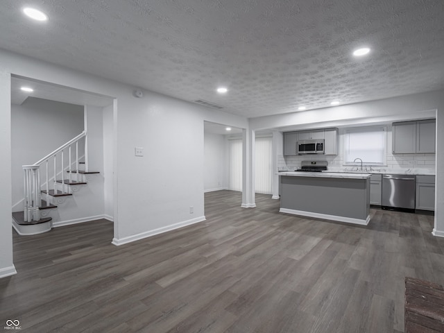 kitchen featuring decorative backsplash, gray cabinets, dark hardwood / wood-style floors, a textured ceiling, and stainless steel appliances