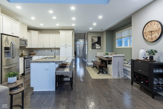 kitchen featuring light stone counters, stainless steel appliances, sink, white cabinets, and an island with sink