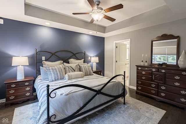 bedroom featuring ceiling fan, dark wood-type flooring, and a tray ceiling