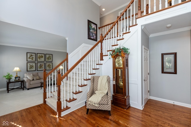 stairs featuring a high ceiling, crown molding, and hardwood / wood-style floors