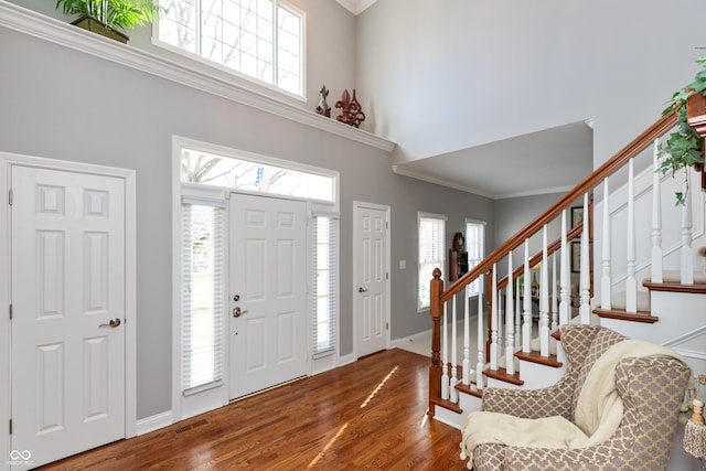 entryway featuring a towering ceiling, ornamental molding, and hardwood / wood-style flooring