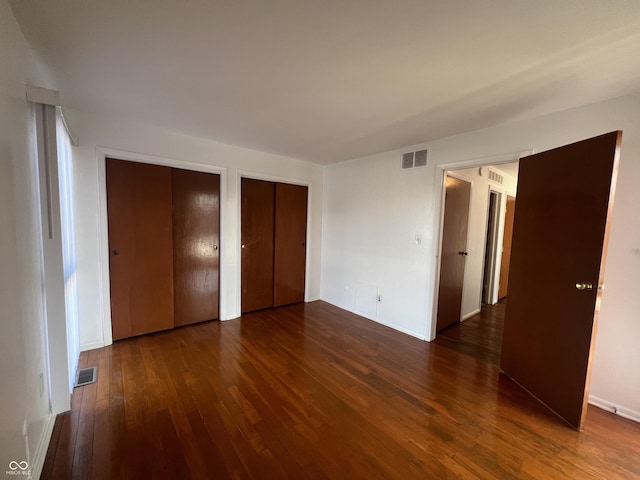 unfurnished bedroom with multiple closets and dark hardwood / wood-style floors