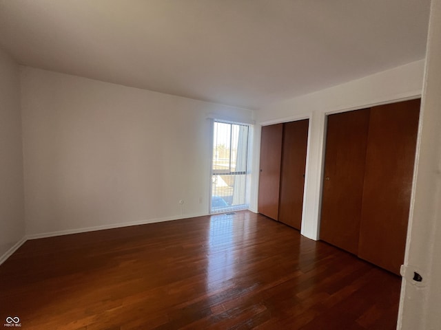 unfurnished bedroom featuring dark hardwood / wood-style flooring and two closets