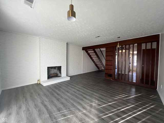 unfurnished living room featuring dark hardwood / wood-style flooring, a fireplace, brick wall, and a textured ceiling