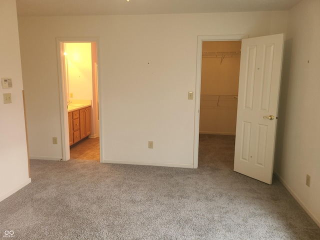 unfurnished bedroom with light carpet, a walk in closet, ensuite bathroom, and a closet