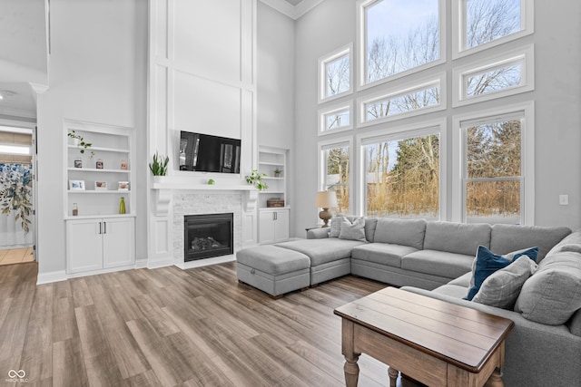 living room with a stone fireplace, light wood-style flooring, crown molding, and built in features