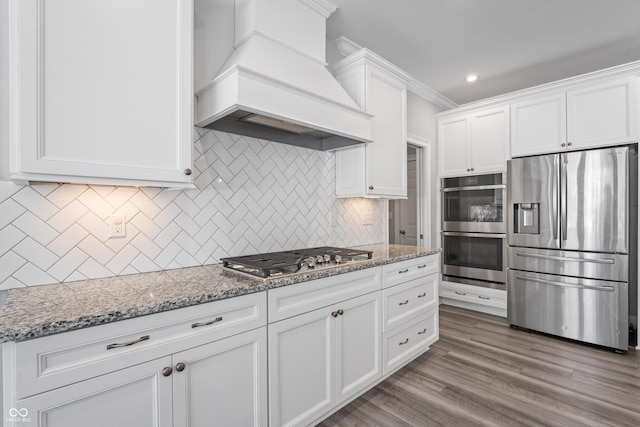 kitchen featuring custom exhaust hood, decorative backsplash, light stone countertops, white cabinetry, and stainless steel appliances